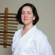 Headshot of Amanda Page, a white woman in her 50s with shoulder-length dark brown hair, smiling and wearing a white gi jacket.