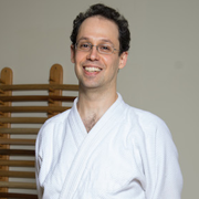 Headshot of Daniel Top, a white man in his 30s with curly dark hair smiling, wearing glasses and a white gi jacket.